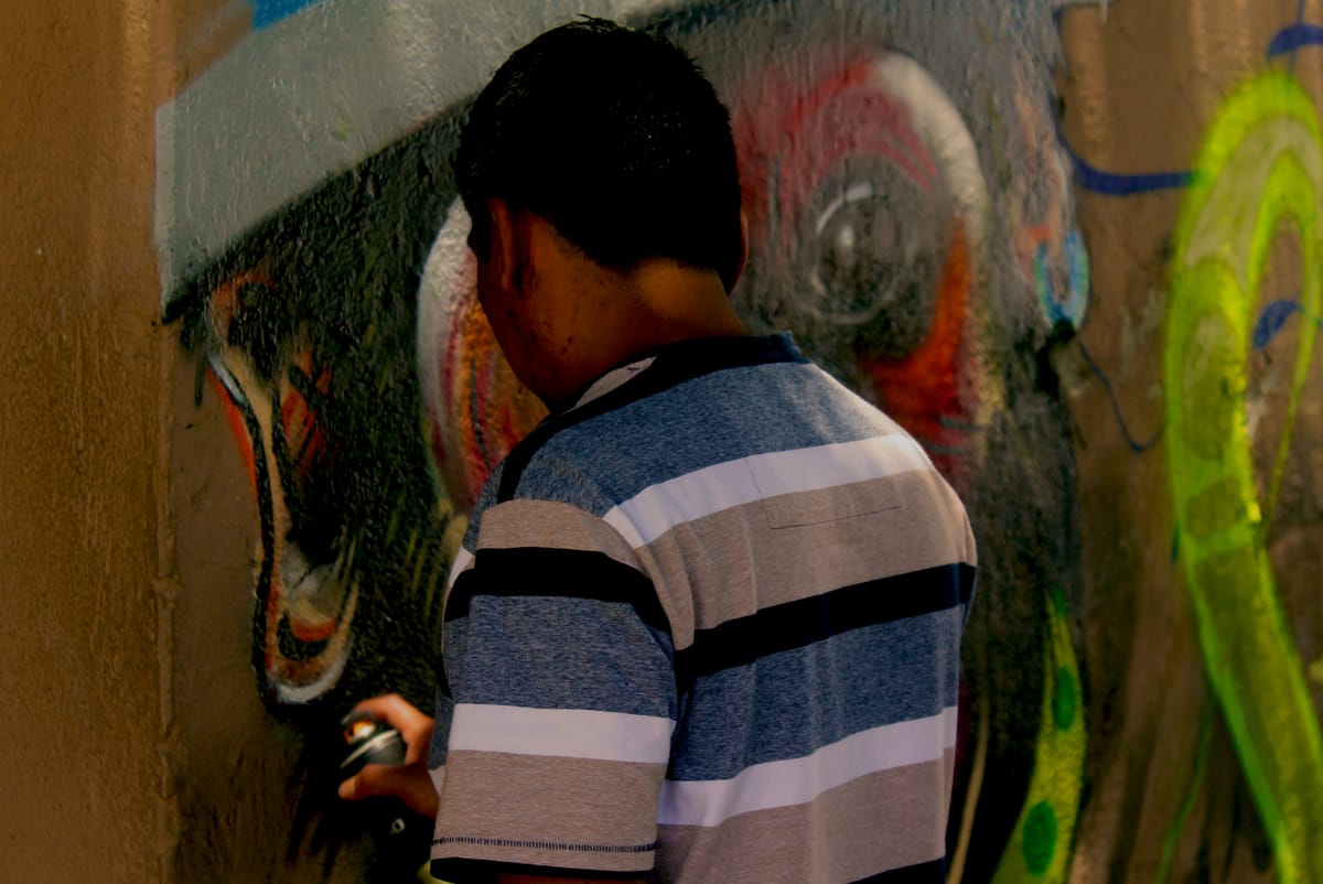 Un artista, visto de espaldas, pintando con aerosol un mural colorido en una pared.