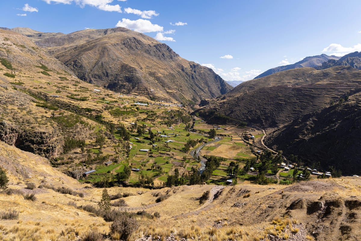 Un valle andino verde con campos en terrazas entre laderas montañosas secas y rocosas.