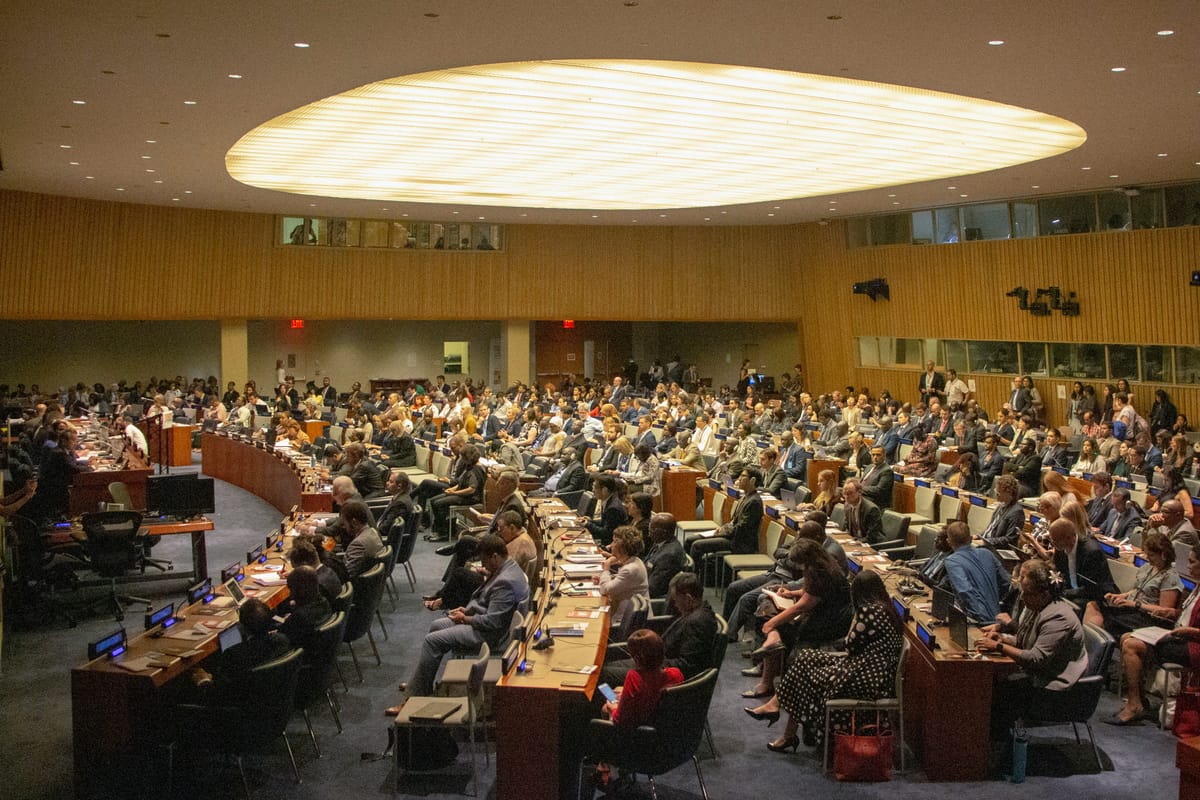 Delegados sentados en filas de escritorios en una gran sala plenaria.