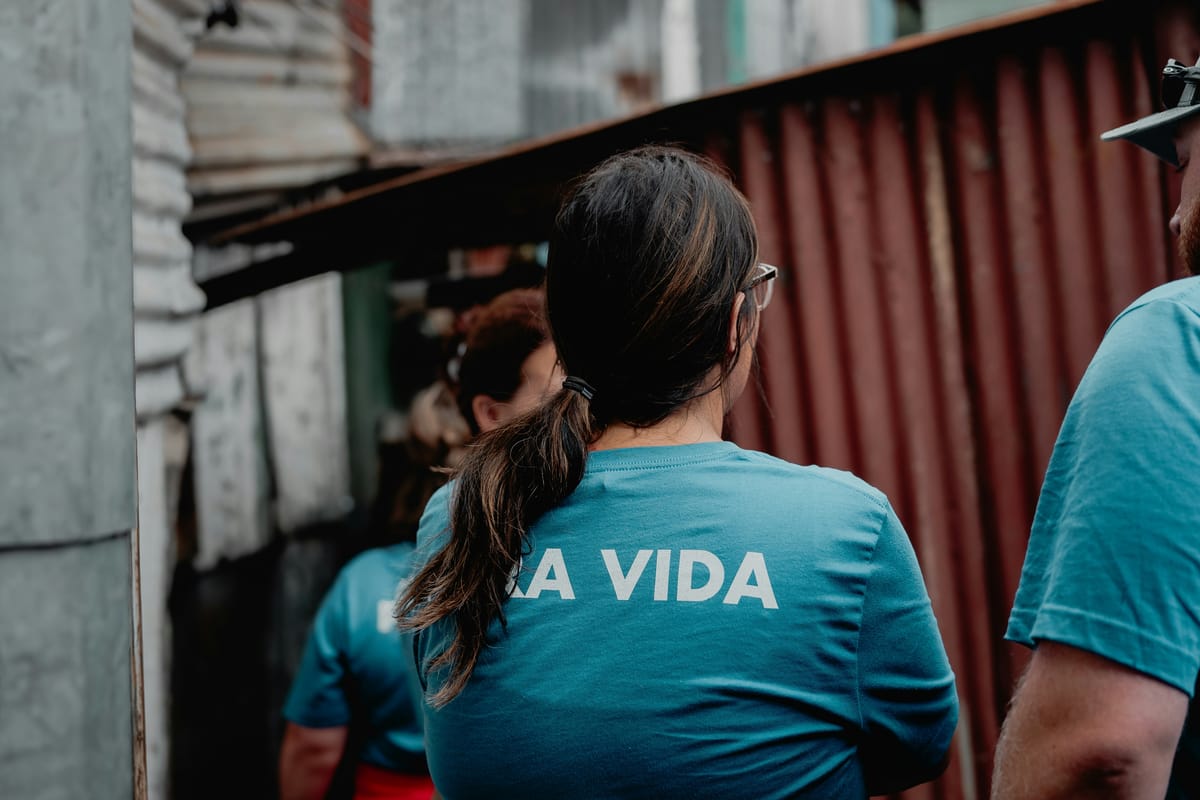 Un equipo con camisetas iguales caminando por un pasaje estrecho entre casas de lámina.